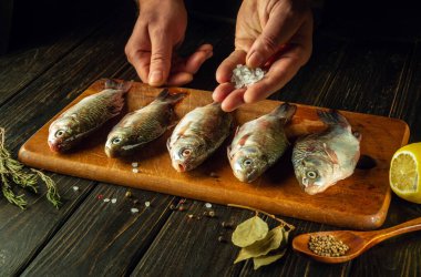 Şefin elleriyle taze balığa tuz ekliyorum. Mutfak masasında baharat ve kişniş ile haç balığı pişirme süreci..