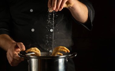 Şef tavuğun bacağını tencerede tuzlar. Lokanta mutfağında lezzetli et suyu hazırlama kavramı ve reklam için siyah bir alan..