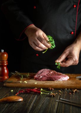 Aşçı lezzetli bir tat için bifteğe aromatik maydanoz ekler. Mutfak masasında dana şiş kebap pişirme kavramı..