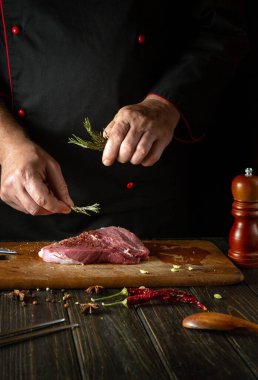 Biberiyeyi, aroma ve lezzet için aşçının eliyle ekliyorum. Mutfak masasında baharat ve biberle biftek pişirme süreci..