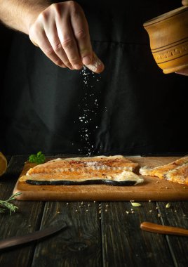 Şef taze somon balığı, alabalık smorgus hazırlar, malzemelere tuz serper. Aromatik baharatlı bir balık yemeği hazırlıyorum. Mutfak masasında somon bifteği..