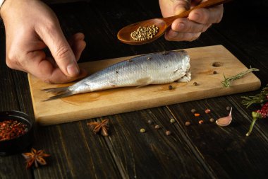 Aşçı lezzetli bir öğle yemeği için mutfak masasında baharat ve kişniş ile Atlantik ringa balığı hazırlıyor. Mutfak masasında çalışma ortamı.
