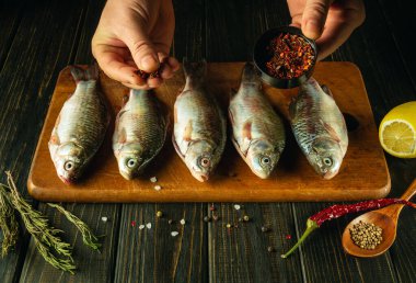 Bir aşçının elleriyle taze çiğ balığa baharat eklemek. Mutfak masasında biberiye ve kişniş ile sazan balığı pişirme fikri..