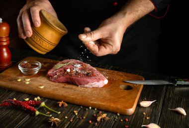 Bir aşçı çiğ bifteğe tuz serper. Izgaradan önce et hazırlıyorum. Bir otel mutfağında çalışma ortamı.