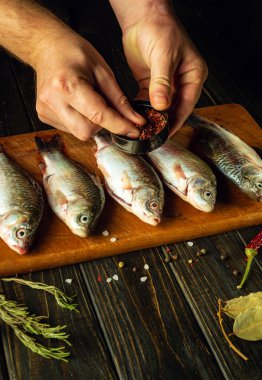 Bir şefin elinden taze balığa baharat eklemek. Mutfak masasında biberiye ve kişniş ile sazan balığı pişirme işlemi..