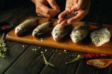 Kesme tahtasındaki çiğ balığa kuru biber ekleyen şefin yakın çekimi. Baharatlı ve biberiyeli sazan balığı pişirme kavramı.