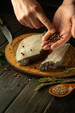 Şef mutfak masasına Anarhichas balıklı bifteğe biber ekler. Baharat ve otlarla lezzetli bir balık yemeği hazırlama fikri..