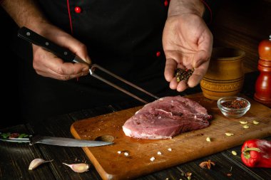 Şef mangal yemeği için çiğ bifteğe biber ekler. Mutfak masasında biberiye ve baharatlarla çalışma ortamı.