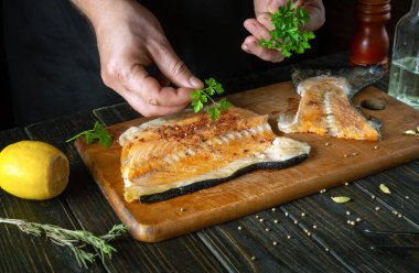 Aromatik baharatlarla tuzlanmadan önce restoranın mutfağında taze kırmızı balık hazırlıyoruz. Şefin eli balık bifteğine maydanoz ekliyor..