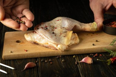 Mutfak masasında tavuk budu hazırlarken bir adamın ellerinin kaşıkla yakın çekimi. Tavuk butuna biber ekliyorum..