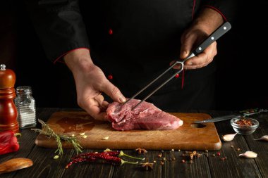 Bir şef bir restoranda mutfak masasında aromatik baharatlı biftek hazırlıyor. Sulu dana etinden barbekü pişirme konsepti.
