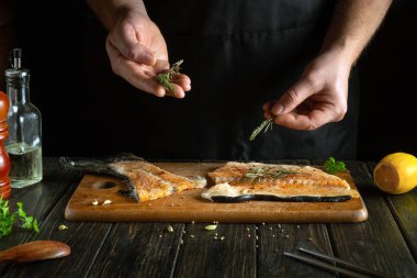 Bir aşçı bir restorandaki mutfak masasındaki taze kırmızı balığa biberiye ekler. Pişirmeden önce balık bifteği aromatik baharatlarla tatlandırılır. Amerikan mutfağı.