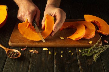 Bir aşçı öğle yemeği için yulaf lapası hazırlamadan önce tahta kesme tahtasının üzerinde bir bıçakla portakal kabağını dilimler. Mutfak masasında vejetaryen yemeği hazırlama kavramı.