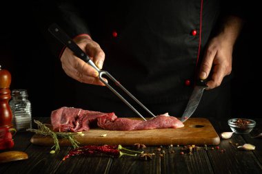 Mutfak masasında biftek pişirme işlemi barbekü için aromatik baharatlarla. Çatal ve bıçak bir aşçının elinde.