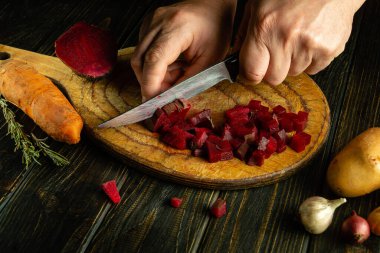 Bıçaklı bir şefin elleri tahta kesme tahtasındaki kaynamış kırmızı pancarlar. Mutfak masasında salata ya da sebze salatası hazırlama fikri..