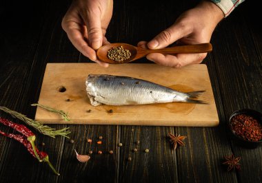 Lezzetli bir akşam yemeği için Clupea balığını baharat ve kişniş ile hazırlama süreci. Mutfak masasında çalışma ortamı. Aşçı çiğ balığa kişniş ekliyor.
