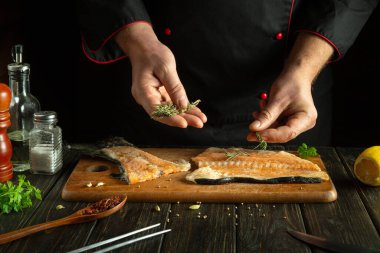 Mutfak masasında kırmızı yağlı balık pişirmek. Aşçı balık bifteğine biberiye ekler. Öğle yemeğinde lezzetli somon balığı.