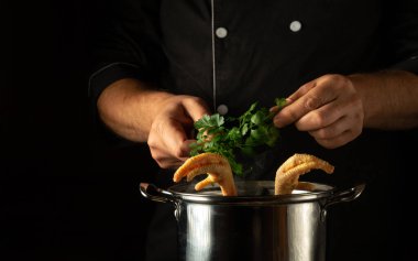 Şef kaynayan tavuk budu tenceresine taze, aromatik maydanoz ekliyor. Siyah arka planda reklam alanı olan restoran mutfağı pişirme kavramı.