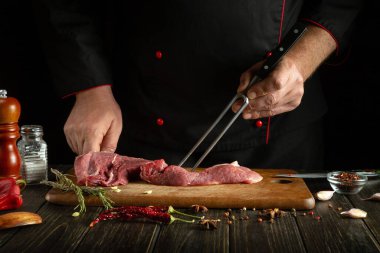 Aşçı mutfak masasında baharat ve biberle sulu bir biftek hazırlıyor. Şefin elini çatalla. Lokantada öğle yemeği için lezzetli ızgara hazırlama kavramı