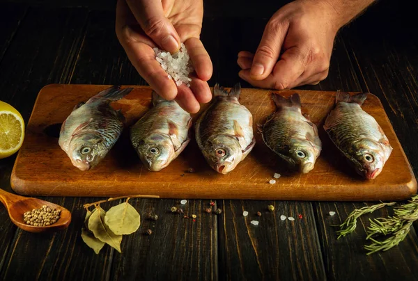 Salting crucian fish with the hands of a chef. Fish menu for a delicious lunch. Fish cooking diet concept on kitchen table