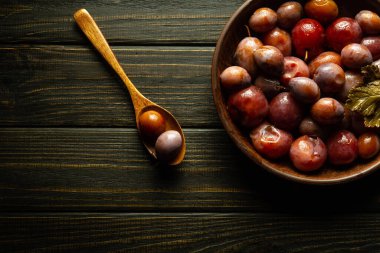 Baharatlı bir kase dolusu erik turşusu ve kırsal, siyah, ahşap bir masada bir kaşık. Lezzetli ve sağlıklı yiyecekler veya vejetaryen gıda konsepti.