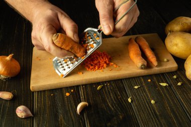 Vejetaryen yemeği hazırlamak için bir şefin ellerinin çiğ havuç rendelemesi. Havuç ve baharatlı sebze menüsü konsepti.