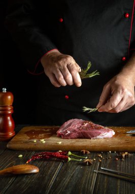 Kızartmadan ya da pişirmeden önce mutfak tezgahında biftek pişirmek. Aşçı bifteğe aromatik biberiye ekler..