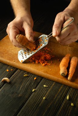 Vejetaryen yemeği hazırlamak için havuç rendeleyen bir şefin ellerine yakın plan. Mutfak masasında sebze pişirme kavramı.