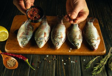 Bir şefin elleriyle taze çiğ balığa baharat eklemek. Mutfak masasında biber ve kişniş ile sazan balığı pişirme işlemi..