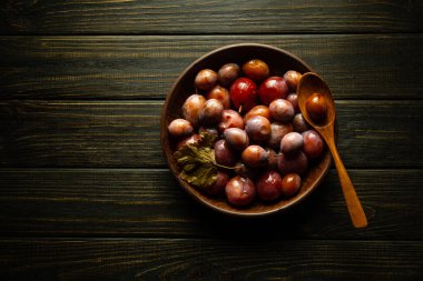Bir kase turşulu erik ve sade, siyah ahşap bir masa. Temiz yemek, vejetaryen yemek konsepti.