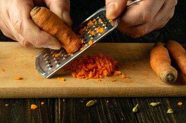 Aşçı yakın plan bir rendeleyiciye havuç sürer. Sağlıklı yeme ve organik ürünler kavramı.