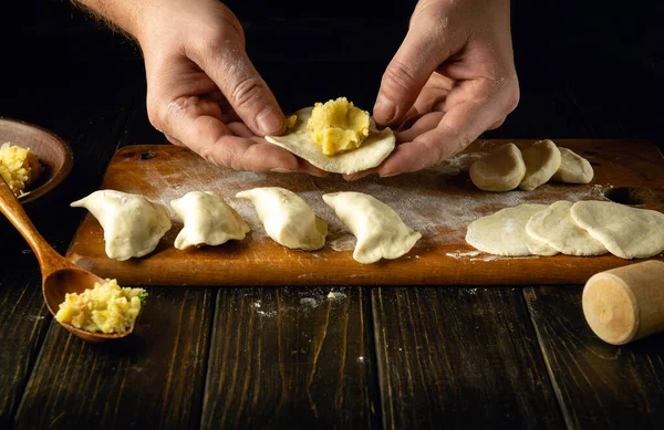 Modeling dumplings by the hands of a chef. The concept of preparing dumplings on the kitchen table from dough and boiled potatoes for a delicious breakfast.