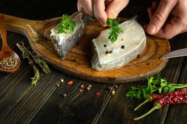 Mutfak masasında bir şefin elleriyle balık bifteği pişirmek. Lezzet ve aroma için maydanoz ekliyorum..