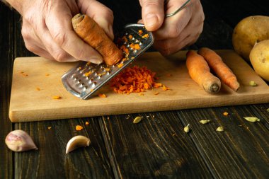 Aşçının elleri rendeleyici ile çiğ havuç rendeliyor. Mutfak masasında sebze salatası hazırlama işlemi..
