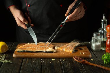 Şef mutfak masasında balık hazırlar ve sonra barbekü bifteğini aromatik baharatlarla hazırlar. Çatal ve bıçak aşçının elinde..