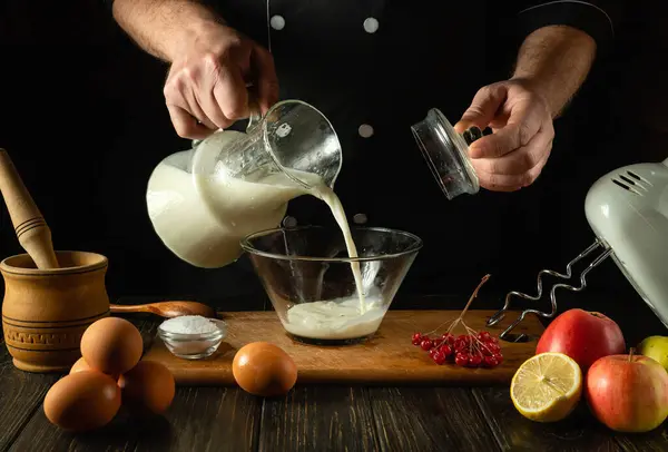 The cook prepares a milkshake with fruits in the kitchen using a hand-held electric mixer. The chef pours milk into a deep plate. Menu of delicious recipes for a hotel.