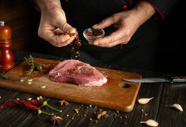 Aşçı mutfak masasında aromatik kuru baharatlı biftek hazırlıyor. Bir şefin elleriyle sulu bir barbekü pişirmek..