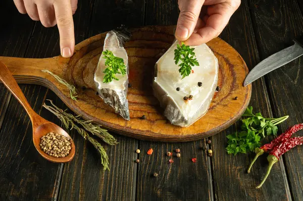 Cooking white fish steaks. The cook adds herbs to raw fish with his hands for aroma and taste before frying.