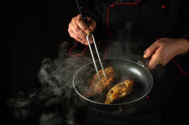 Aşçı, restoranın mutfağında tavada sazan balığı kızartıyor. Siyah arka planda lezzetli bir balık diyeti fikri. Şefin elini çatalla..