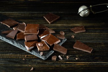 Koyu renkli bir masada kırılmış siyah çikolata parçaları ve çikolata parçaları için mutfak süzgeci. Tatlı mı yoksa atıştırmalık mı?.