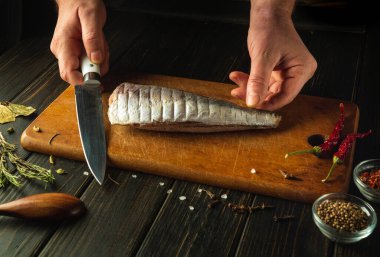 Tahta kesme tahtasındaki hake balığını kesmeden önce adamın elleri bıçakla bağlanmış. Yemek için mutfak masasında balık yemeği pişirme kavramı..
