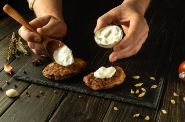 Şefin elleriyle kızarmış pirzolaya nefis bir tat katmak için ekşi krema ekliyorum. Bir ziyafette lezzetli bir et yemeği sunma süreci..