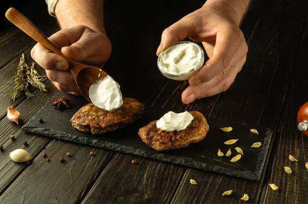 Şefin elleriyle kızarmış pirzolaya nefis bir tat katmak için ekşi krema ekliyorum. Bir ziyafette lezzetli bir et yemeği sunma süreci..