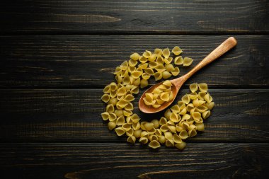 Antika karanlık bir masada kabuklu makarna ve kahvaltı hazırlamadan önce kaşıkta. Yemek tarifi ya da restoran menüsü için yer.