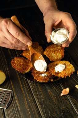 Şef patatesli gözlemelere tatları için bir kaşıkla ekşi krema ekler. Kahvaltı için sebze yemeği hazırlama kavramı.