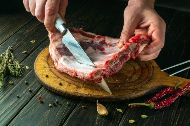 Bir aşçı et yemeği hazırlamadan önce çiğ kaburgaları kesme tahtasıyla keser. Bir otel tarifi fikri..