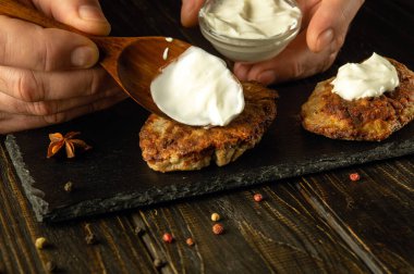 Aşçının elinde ekşi kremalı kaşık. Pirzola ve ekşi kremayla atıştırmalık bir şeyler hazırlıyorum. Gıda hizmeti kavramı.