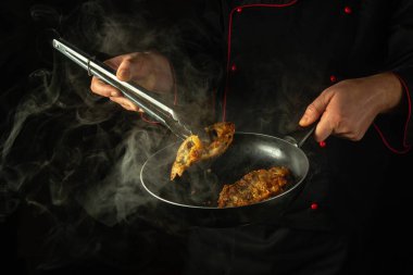 Aşçı kızgın balığı kızartma tavasından çıkarmak için maşa kullanır. Otel ya da restoran mutfağında lezzetli bir balık yemeği hazırlama kavramı.