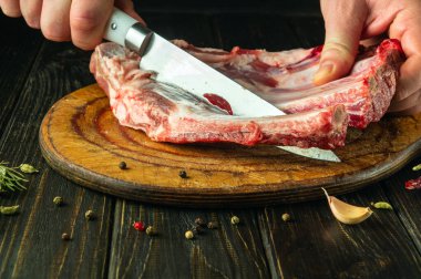 Aşçı ahşap bir tahtanın üzerinde bir bıçakla çiğ kuzu kaburga keser. Et yemeği veya kebap hazırlama süreci konsepti. Asya mutfağı.