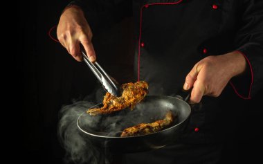 Restoran mutfağında balık yemeği hazırlıyorum. Aşçı kızartma tavasında balık kızartır. Reklam için siyah alan.